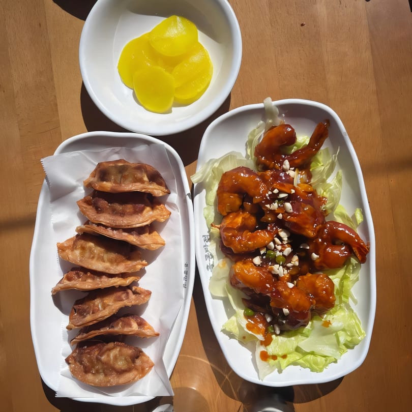 Korean fried dumplings, sweet and sour shrimp, and pickled radish on a wooden table.