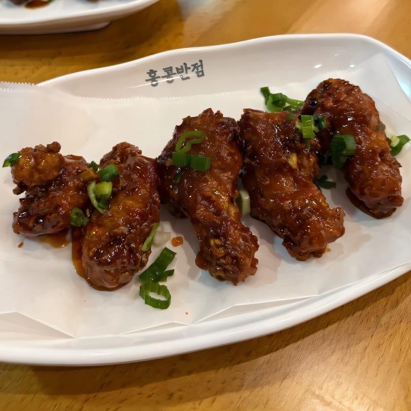 Five Korean fried chicken wings, glazed in a rich brown sauce and garnished with green onions.